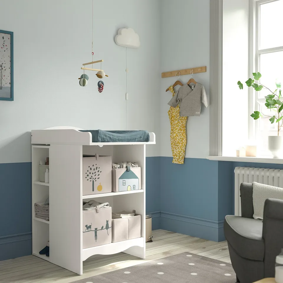 Kids room with SMÅGÖRA changing table, toys, baby clothes, chair, plant.
