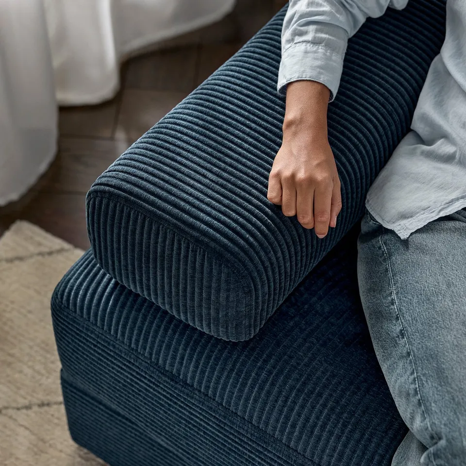 A person on a navy-blue, cushioned sofa holding the armrest.