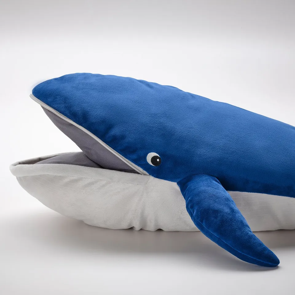 A blue whale-shaped pillow with a zip and realistic eye, part of the BLÅVINGAD collection, designed for comfort and safety.