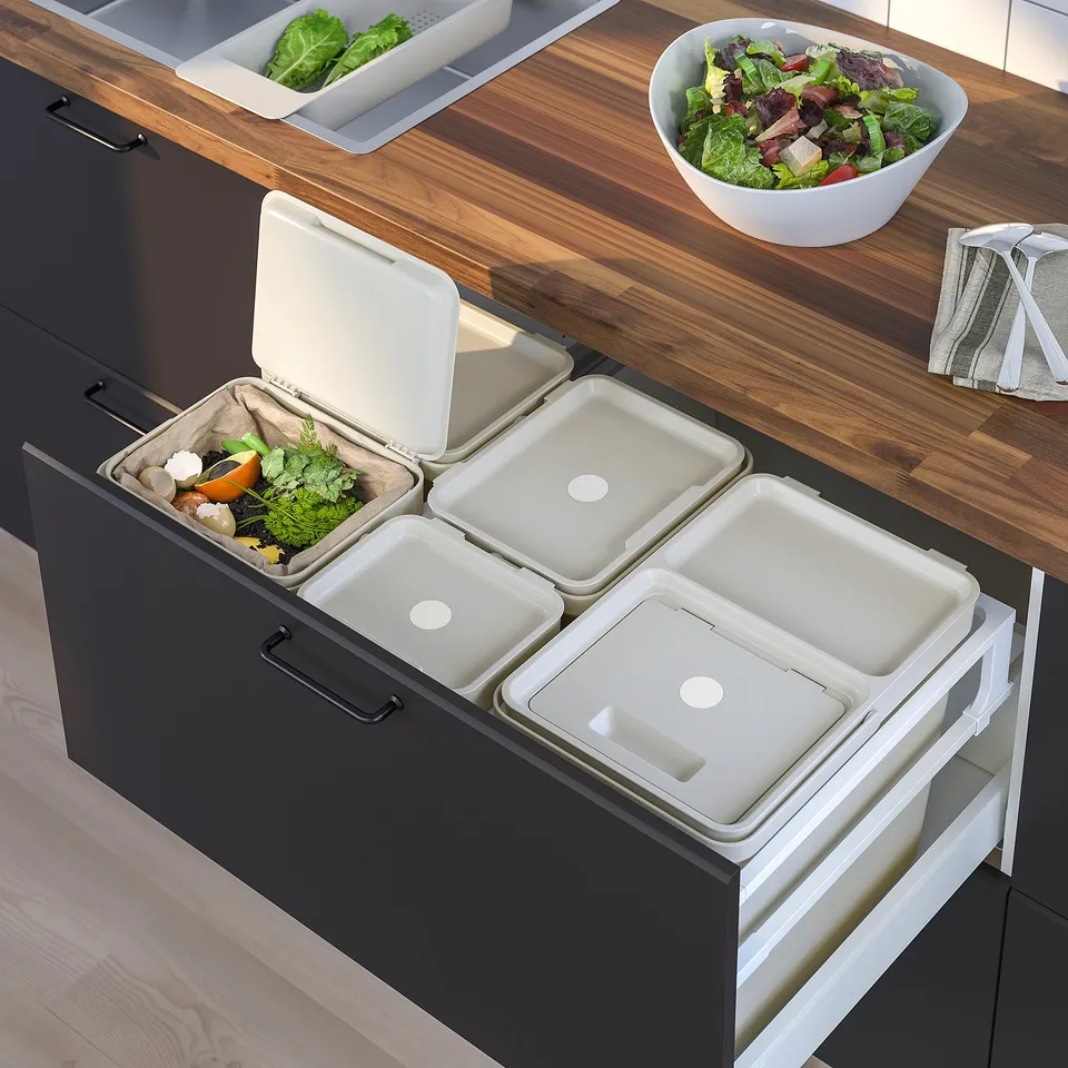 Modern kitchen with pull-out recycling bins. Bins in dark cabinet, wooden countertop with salad bowl.