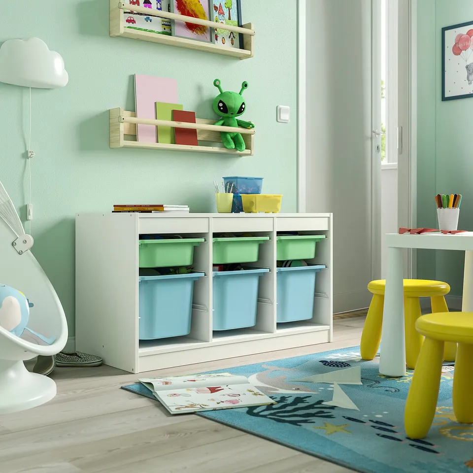 Kids playroom with white TROFAST storage, green walls, and rug. Toy alien, plastic boxes, and stools.