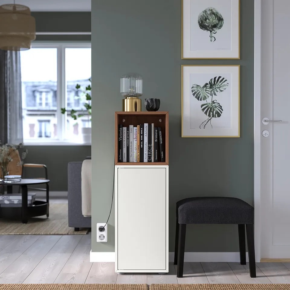White storage cabinet against a grey wall, holding books and decor, next to a black stool and a doorway.