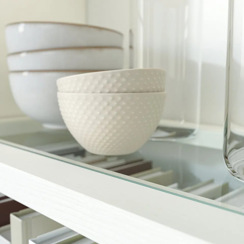 White wooden cabinet with glass shelf, holding stacked white bowls.
