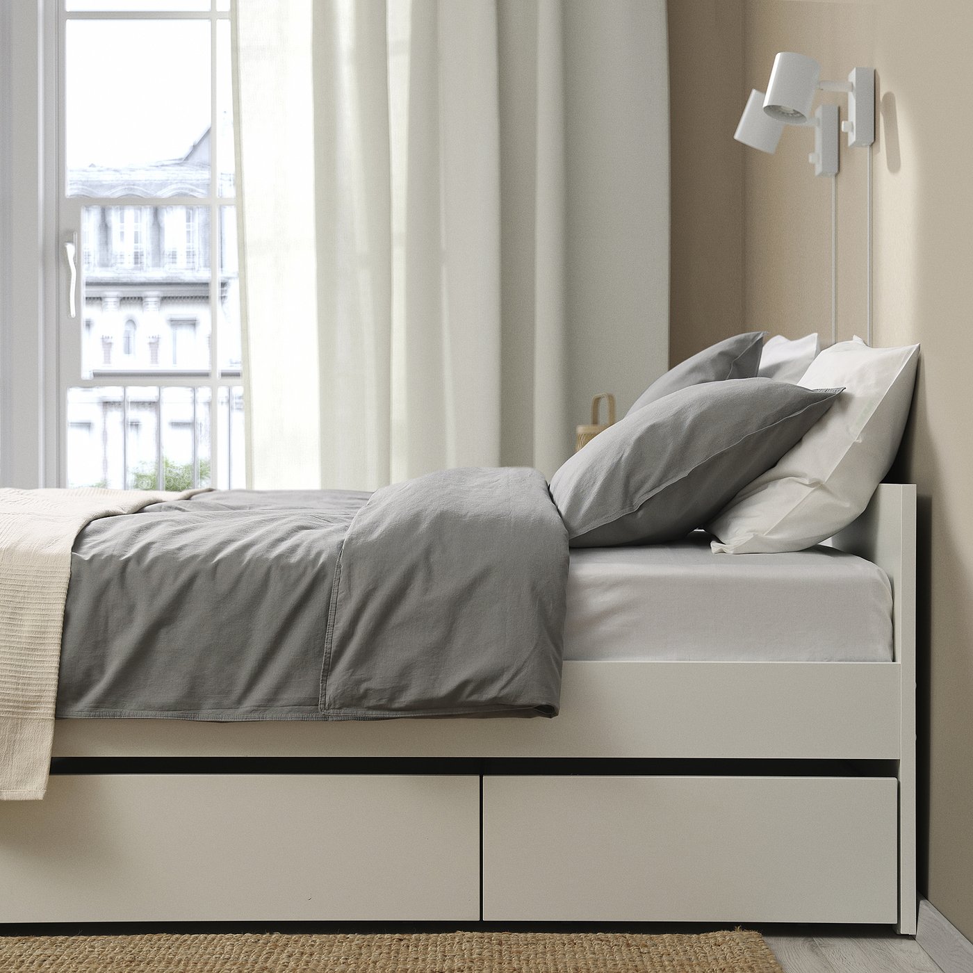 Modern bed frame with built-in storage. Grey bedding set and headboard visible. Window with city view in background.