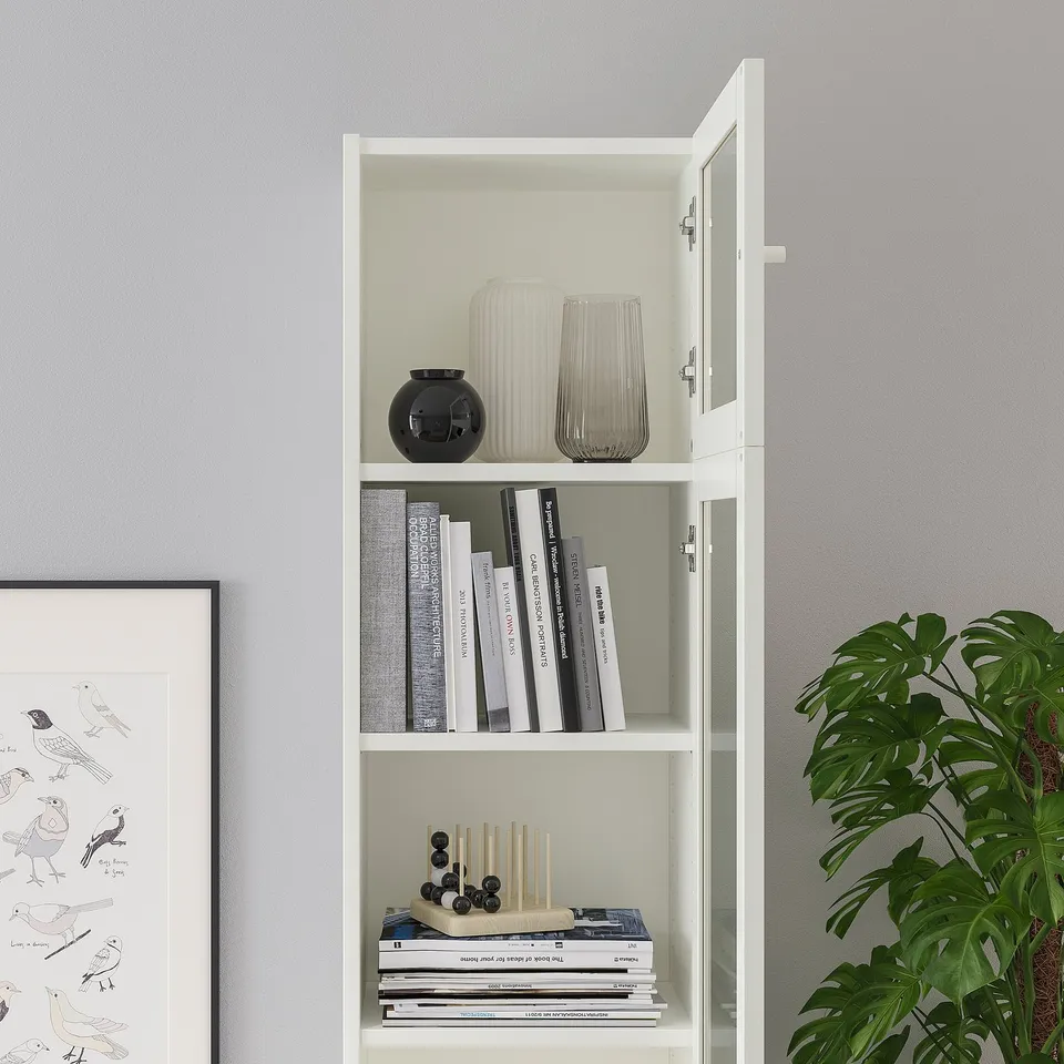 White BILLY bookcase with glass door, displaying vases and books. The glass door allows for dust-free storage and showcasing items.