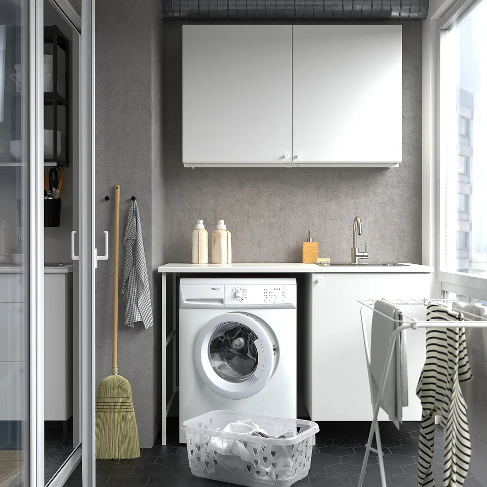Small, modern laundry setup with white ENHET cabinets, sink & washing machine. Tidy design, efficient use of space.