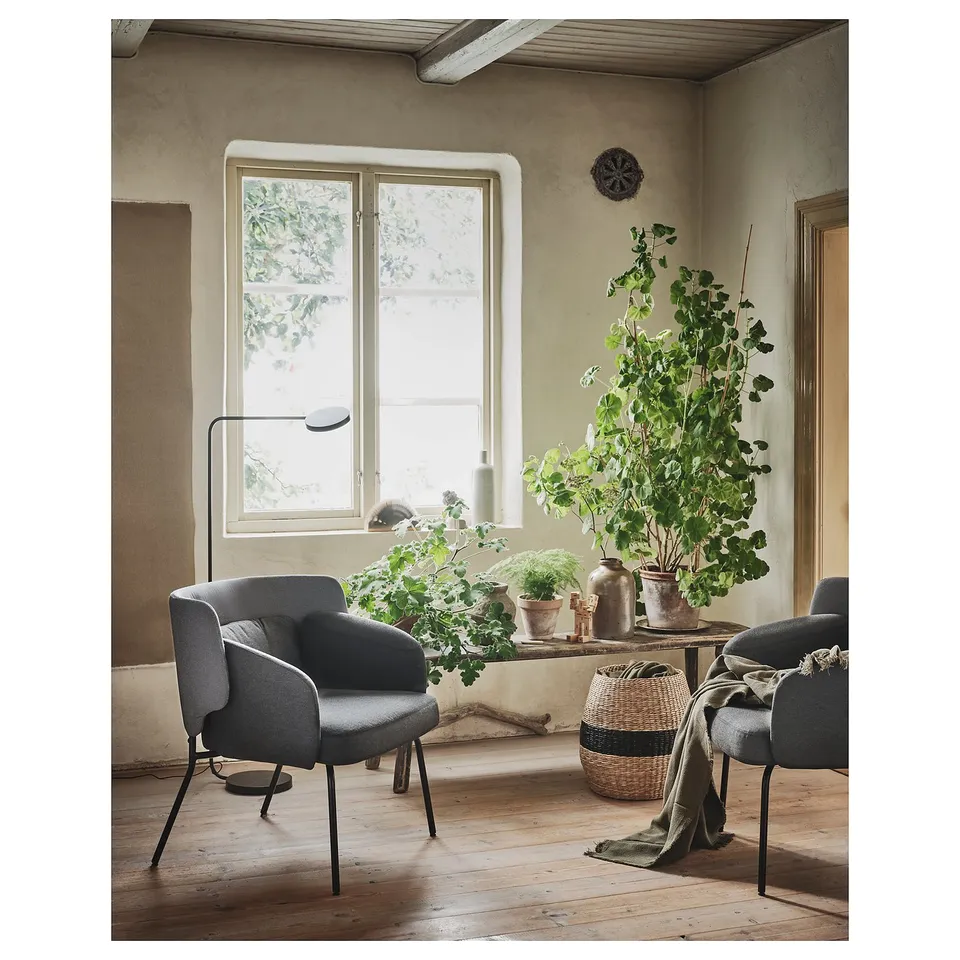 Cosy room with BINGSTA grey armchair, large window, plants, natural wood floor, rustic decor.
