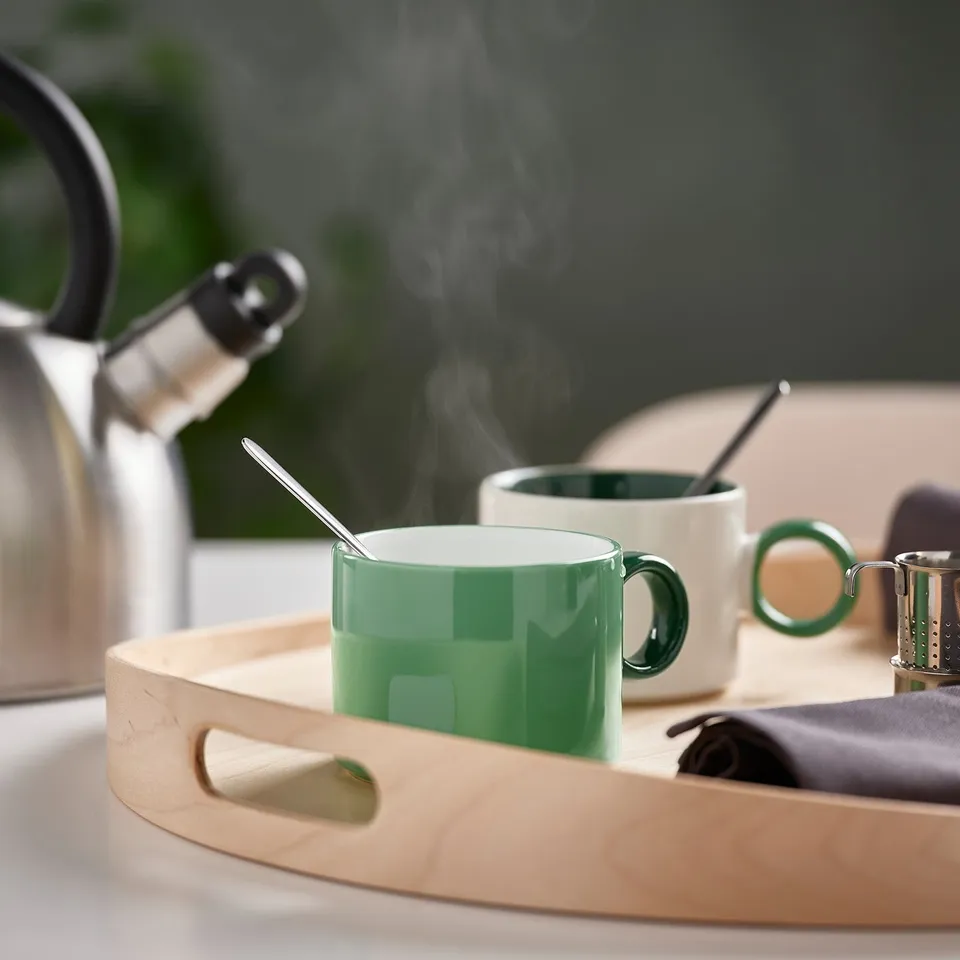 Two green mugs on a wooden tray with steam rising, perfect for coffee or tea.