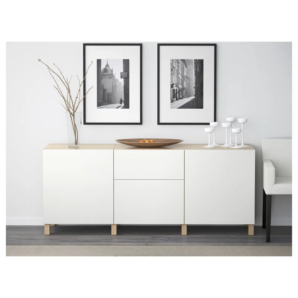 White modern cabinet with framed black & white photos, branches in a vase, wooden bowl, and wine glasses on top. Soft-closing drawers, wall-fixed.