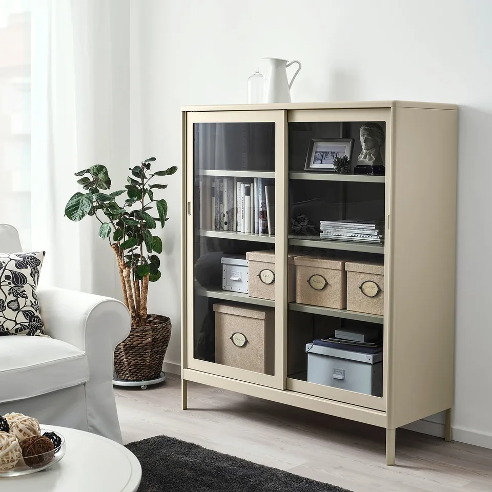 Beige IDÅSEN cabinet with glass doors saves space, housing books and more.