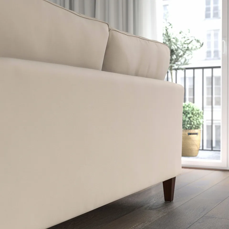 A modern beige sofa with wooden legs sits near a window. The sofa a clean, elegant design and is part of the EKHOLMA collection.