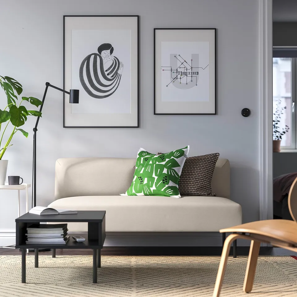 Contemporary living room with beige sofa, green cushions, grey wall, art, plant, side table with books, rug, chair, and lamp.