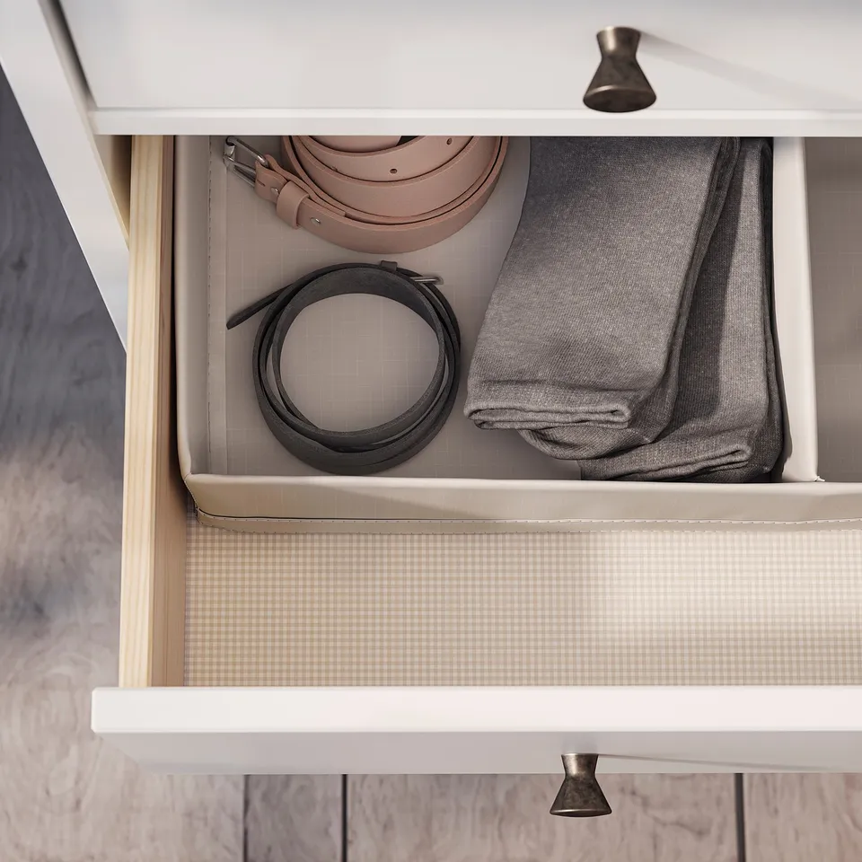 White dresser drawer organised with rolled belts and folded grey clothing.