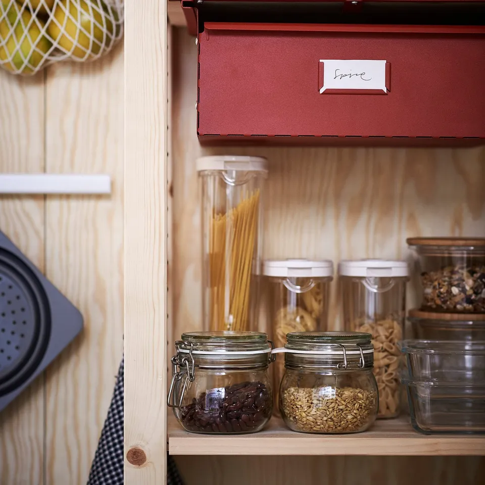 Organisation of kitchen items in wooden cabinets. Glass jars, one with dried fruits, another with grains, stored on shelves.