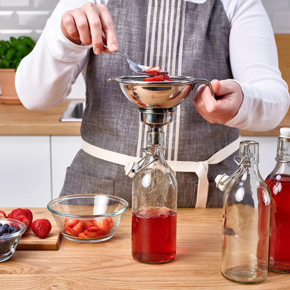 Straining fruit juice into bottle with strainer, strawberries nearby.