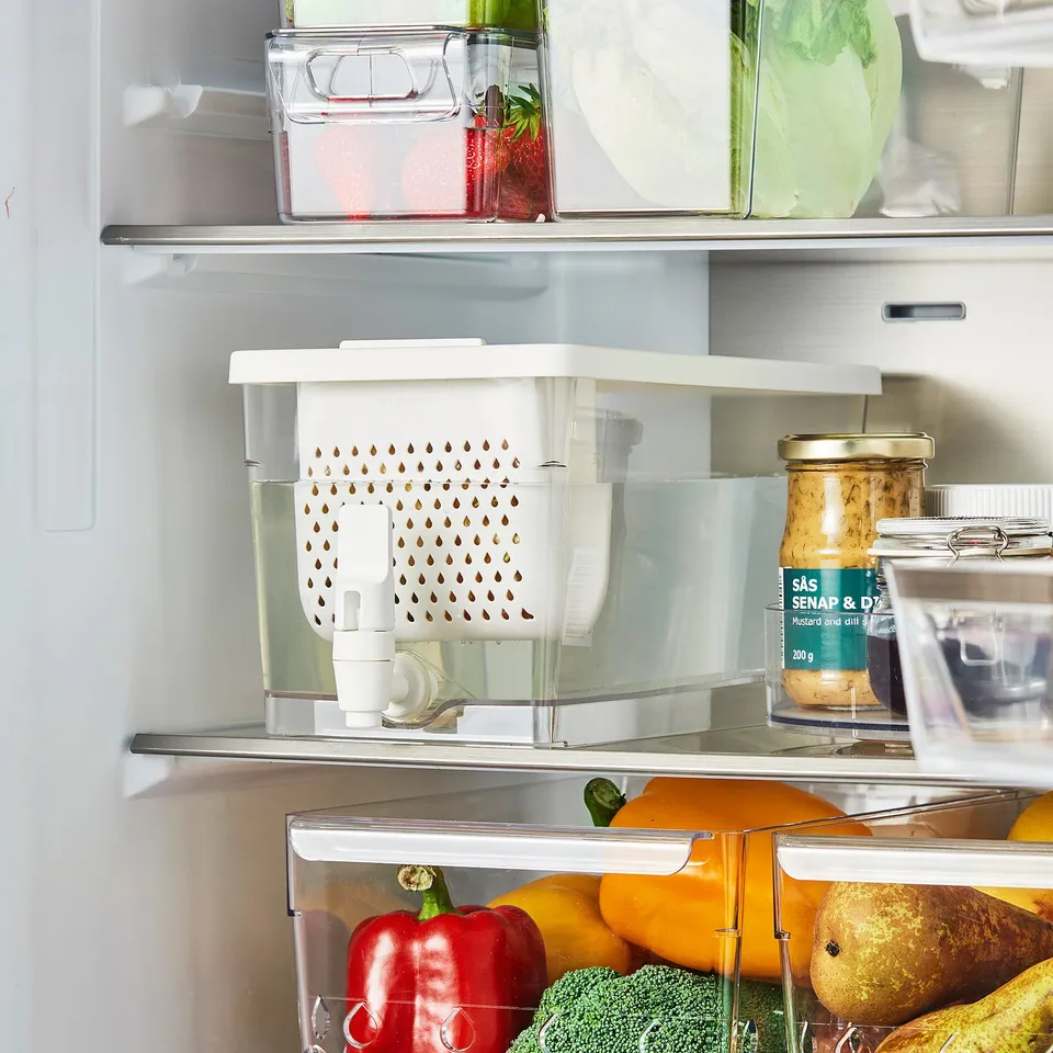 Open fridge with veggies, jar, and a clear box with KLIPPKAKTUS tap for chilled drinks.