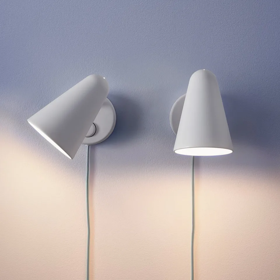 Two modern, wall-mounted lamps with adjustable shades, one lighted, emitting warm white light.