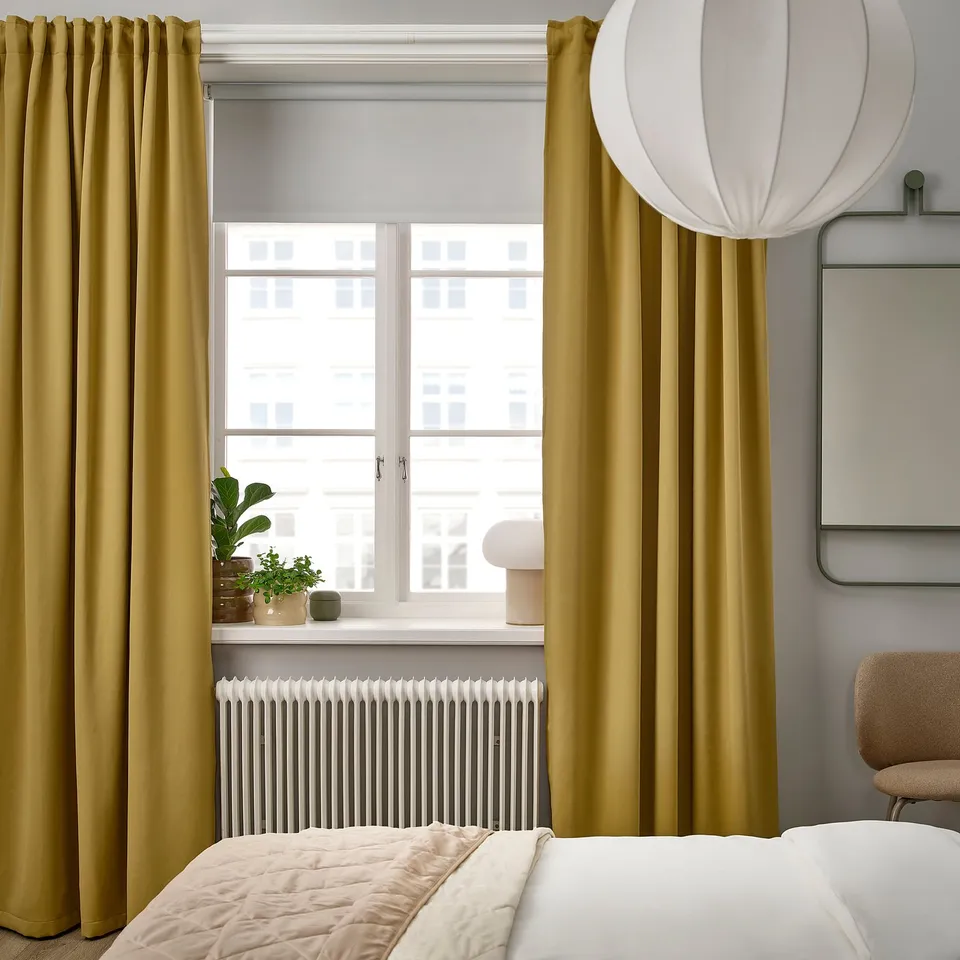 Modern bedroom with MAJGULL curtains, white radiator, city view window, pendant light, cosy bed, and chair by a mirror.