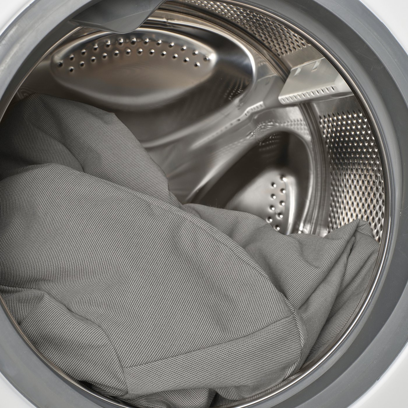 Washing machine cleaning a grey item. Steel drum has drainage holes.