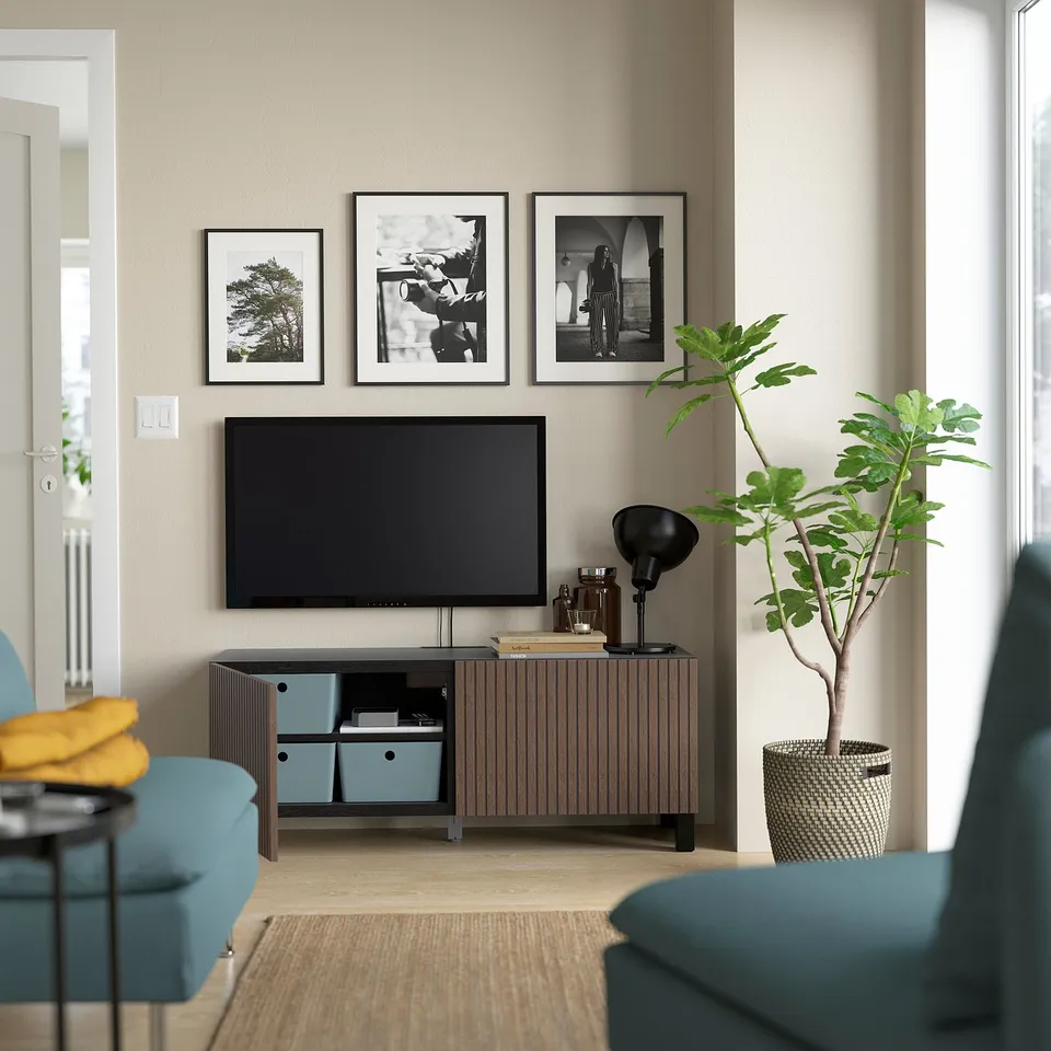 Modern living room with beige walls, featuring a BESTÅ tv bench holding a flat-screen tv, surrounded by decorative items and plants.