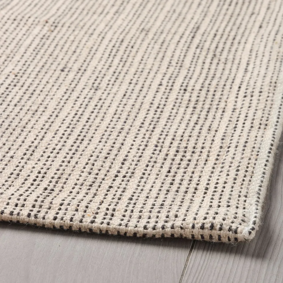 Beige and grey woven cotton rug with intricate diagonal stripes, laid on a wooden floor.
