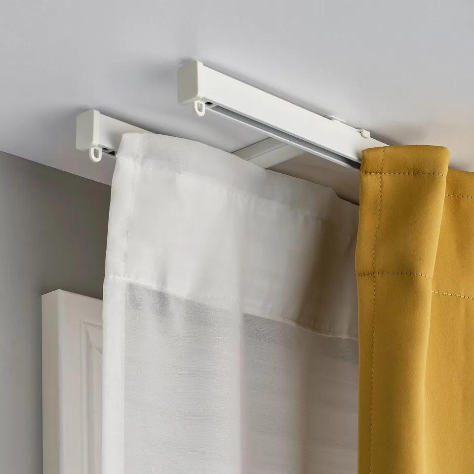 White curtain gliding on ceiling-mounted rail. Two-layer solution with mustard curtain behind.