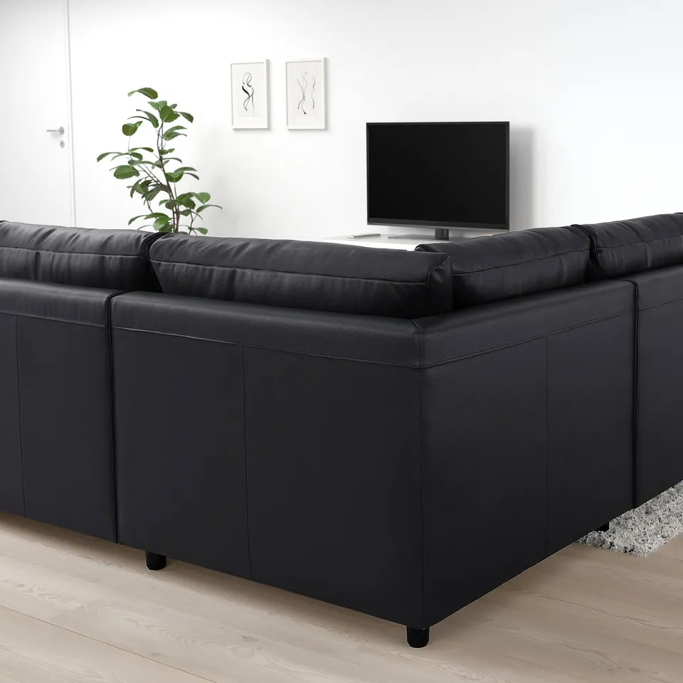 Black leather VIMLE sectional sofa in minimalist room. Plant on left, tv in front, light wood floors, white walls.