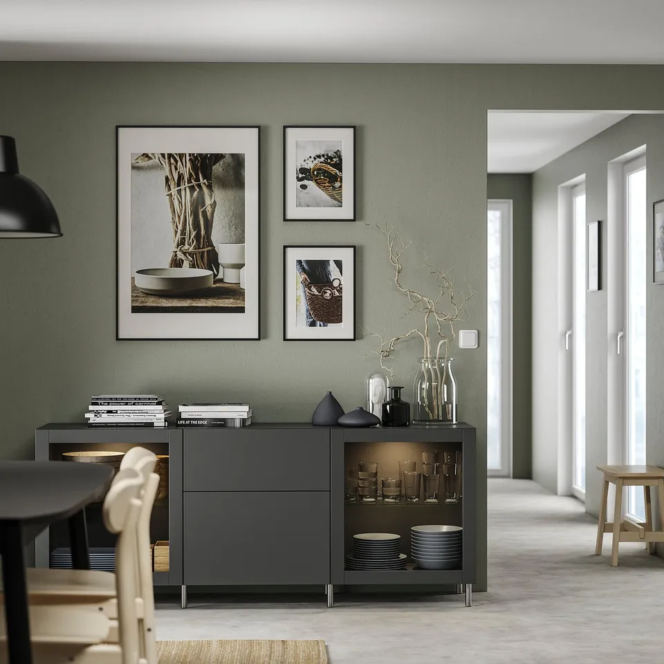 Modern living room with green walls, featuring a black BESTÅ furniture unit, decorated with vases and framed art.