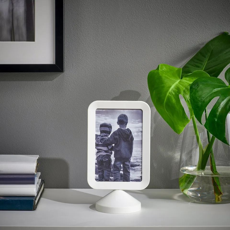 Photo frame displaying a picture, sits on a desk beside books and a plant.
