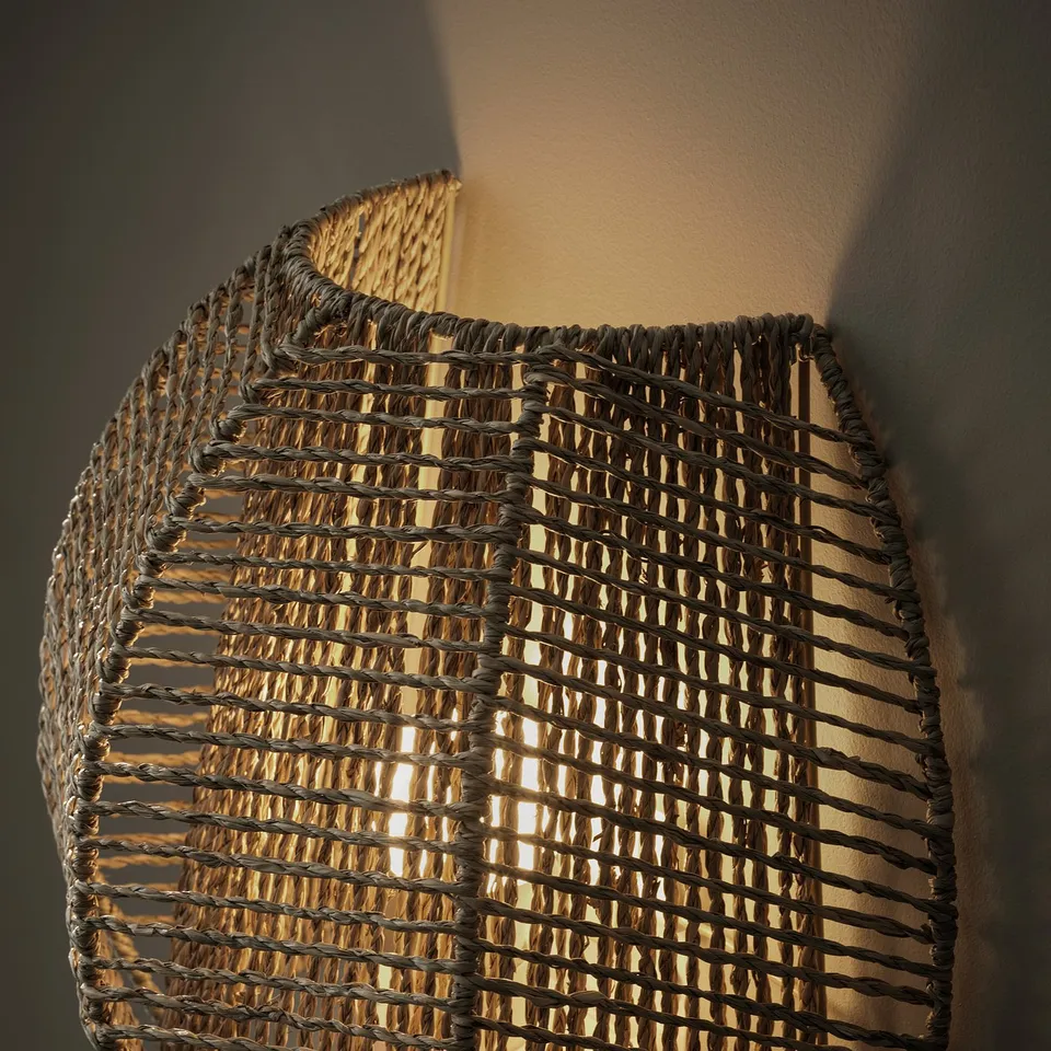 Hand-braided wall lamp with natural sedge material, emitting warm decorative light.