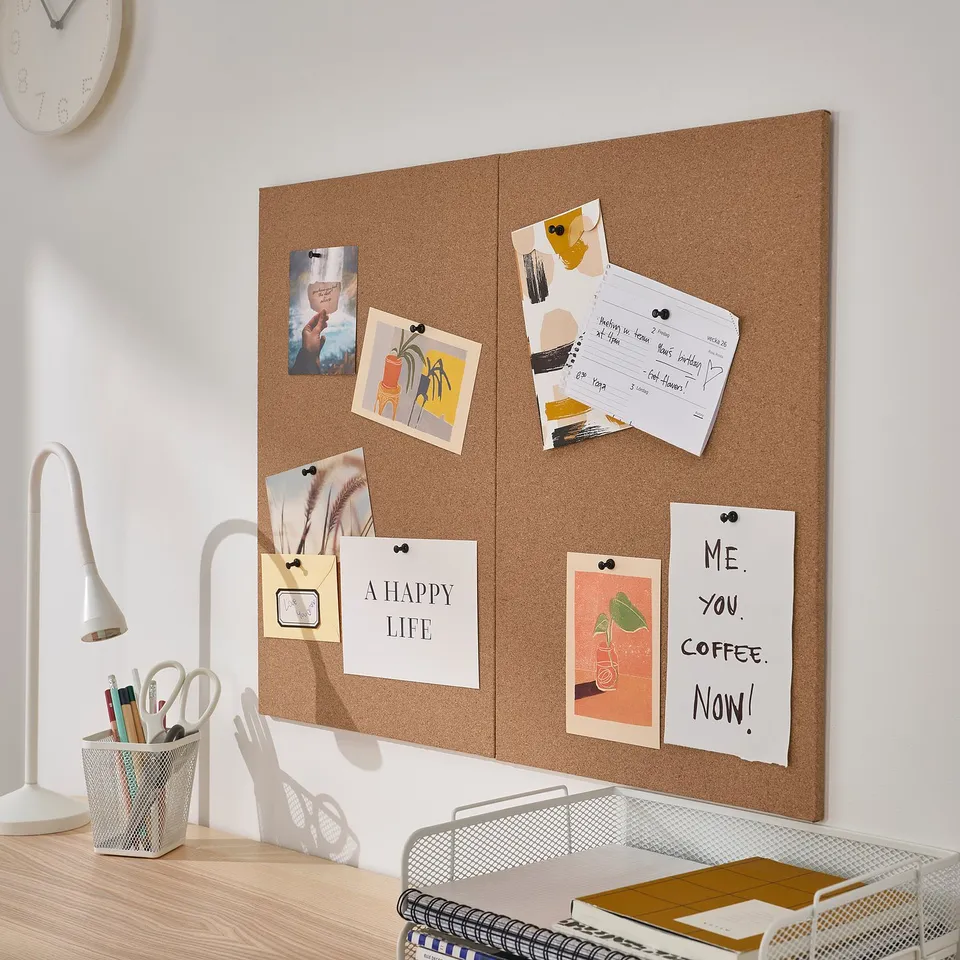 Cork board on wall with photos, notes, lamp, notebooks, pens.