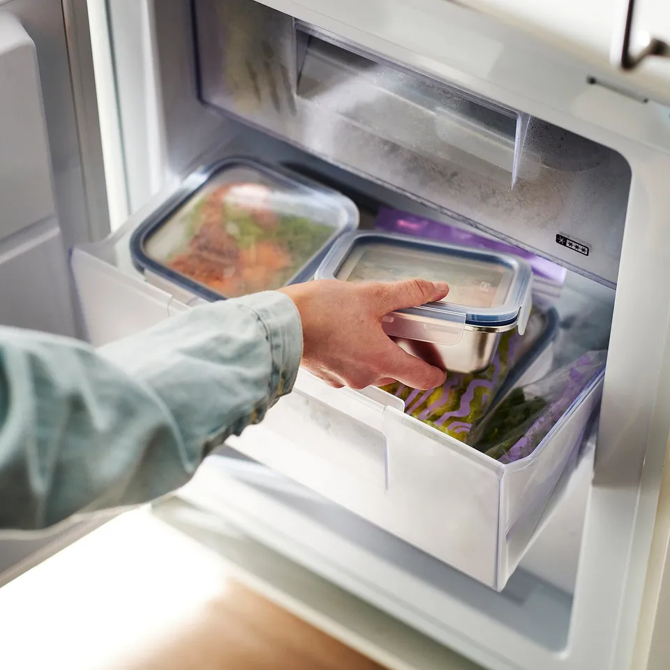 Person taking stainless steel food container from fridge drawer.