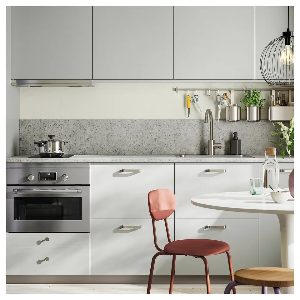 Modern kitchen with white cabinets, stainless steel appliances, hanging utensils, a red chair, and a small island with glassware and plants.
