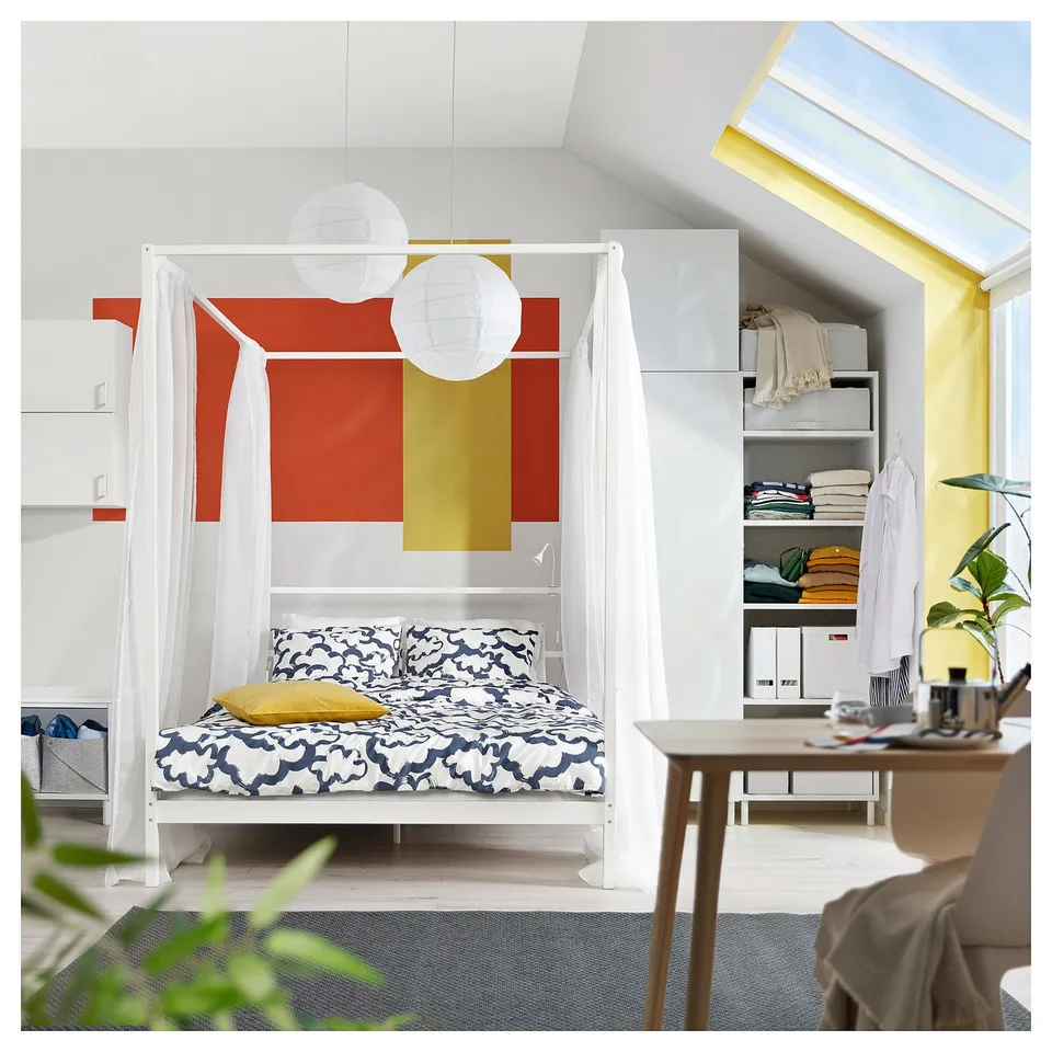 Modern bedroom with VITARNA bed, blue bedding, yellow pillow, and sheer curtains. Bright, organised.