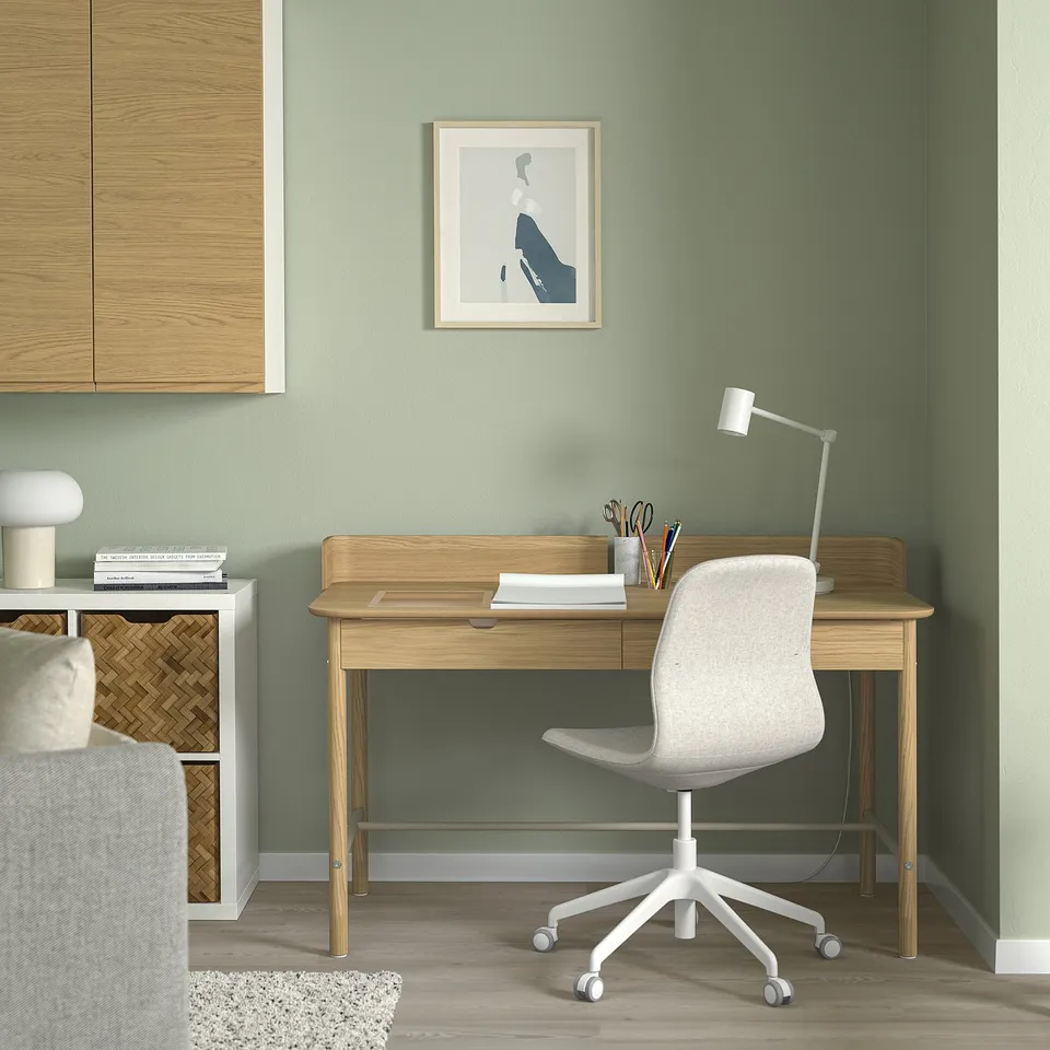Minimalist home office: light wooden desk with white chair, lamp, and painting.