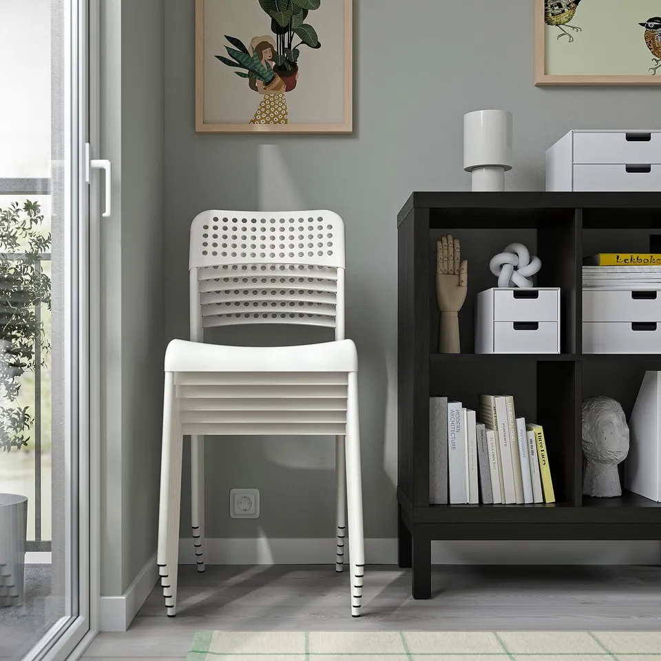 Stackable white chair near shelf with books. Indoor use only.