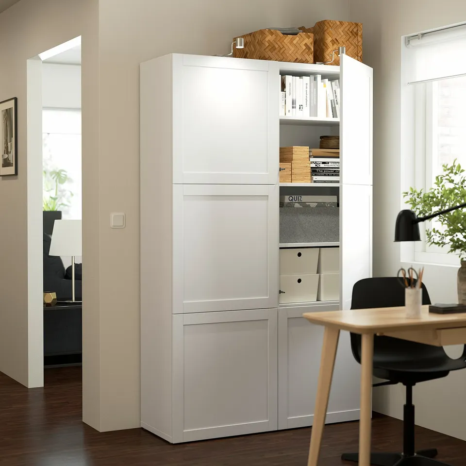 White storage unit with open doors, displaying shelves with books, boxes, and a basket on top, set in a home office with a desk and chair.