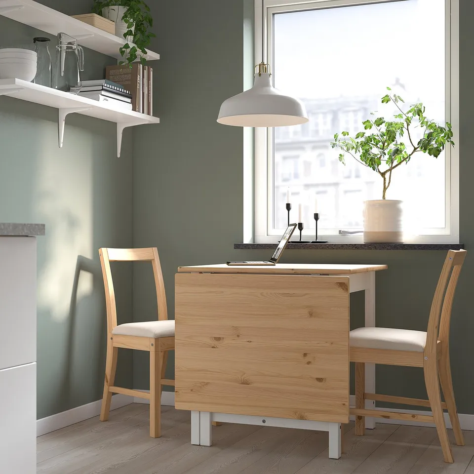 Light wood drop-leaf table for 2-4, nestled between shelves and window, with cosy chairs.