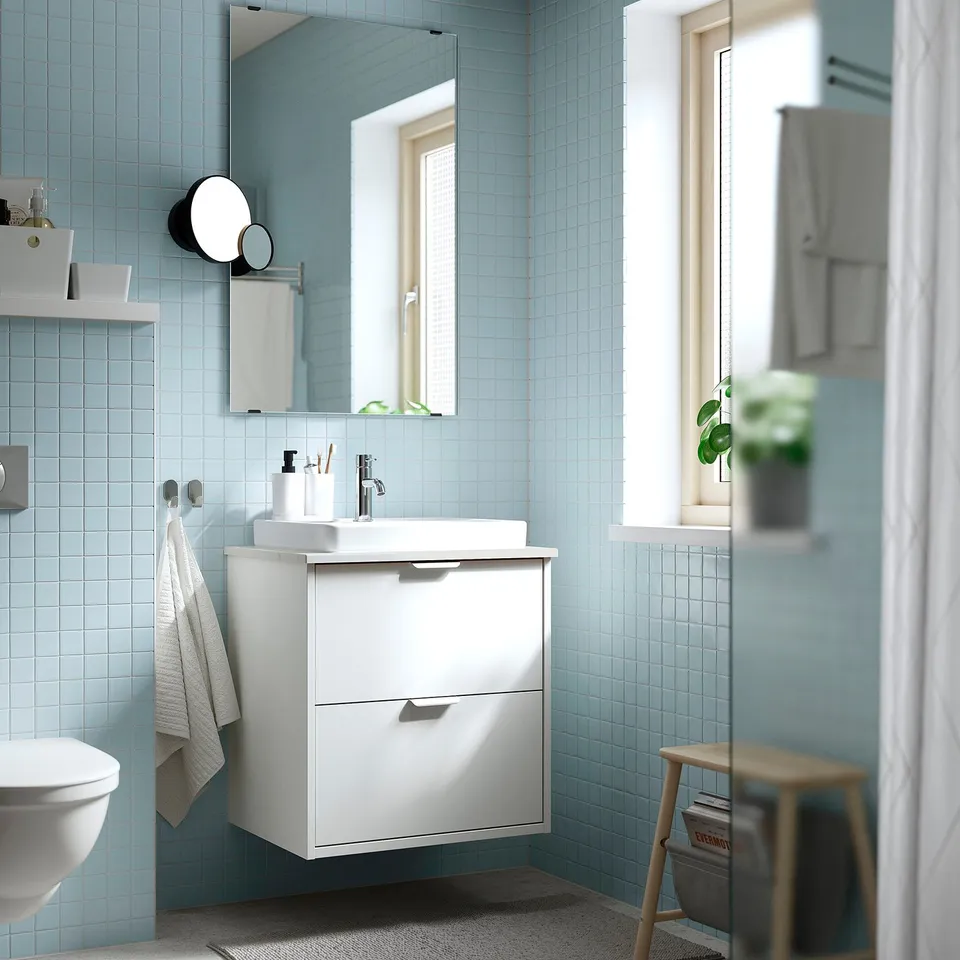 Modern bathroom with light blue tiles. White HAVBÄCK vanity, clean lines, semi-recessed basin, wall-mounted. Mirror above, towels hung nearby.
