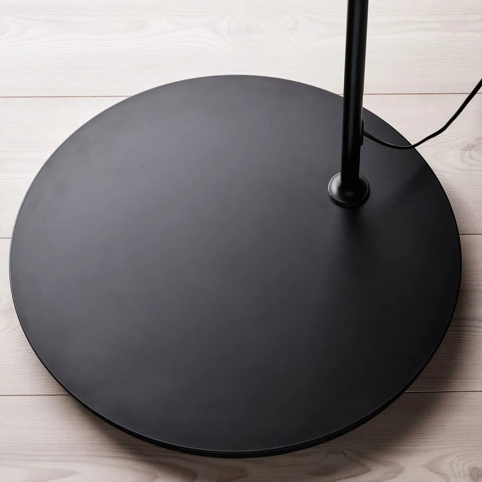 Large black circular lamp base on wooden floor, with sleek design and central support.