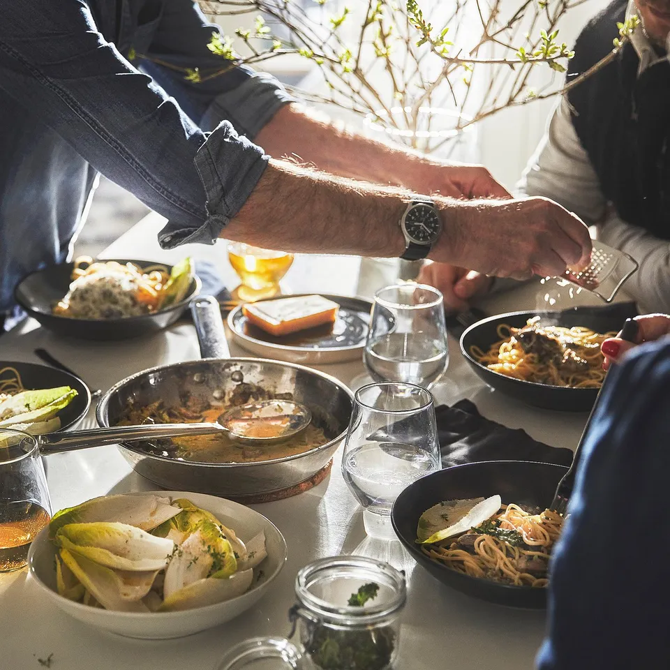 People enjoying a meal, hand with watch holding pepper mill.