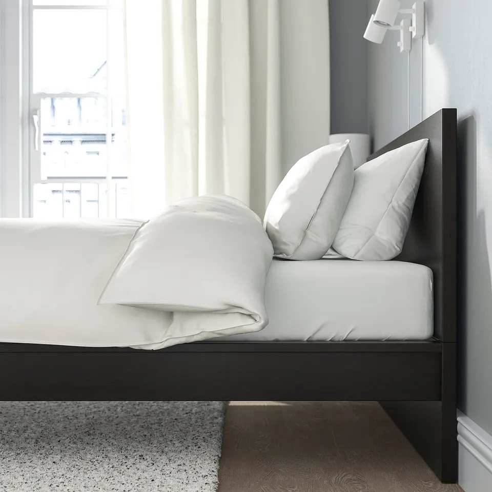 Modern bed with clean design, high headboard, and adjustable bed sides. White bedding, dark wood frame, and large window with curtains.