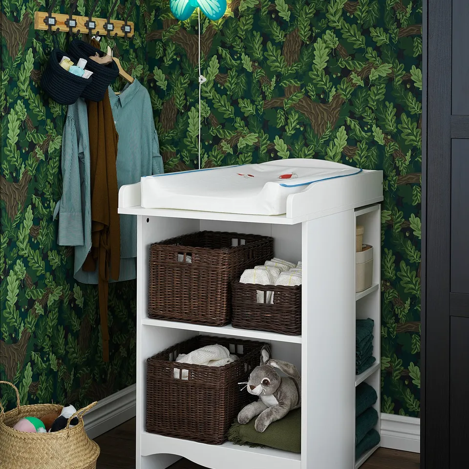 SMÅGÖRA changing table shelf with wicker baskets and stuffed animal.