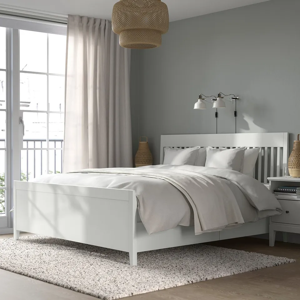 Minimalist white bed, grey linens, lamps, large window, area rug, blue-grey walls, woven light.
