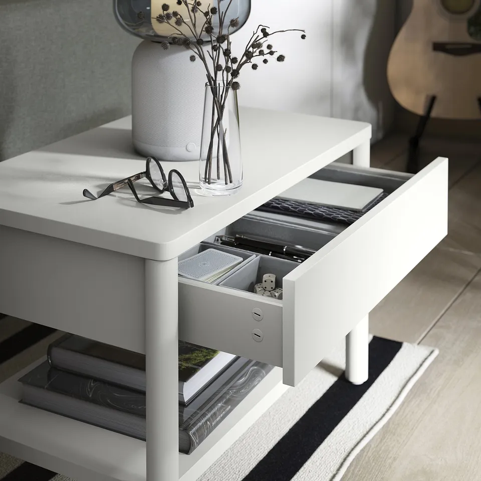 Off-white TONSTAD side table with drawer and shelf, holding glasses and vase, on a striped rug.