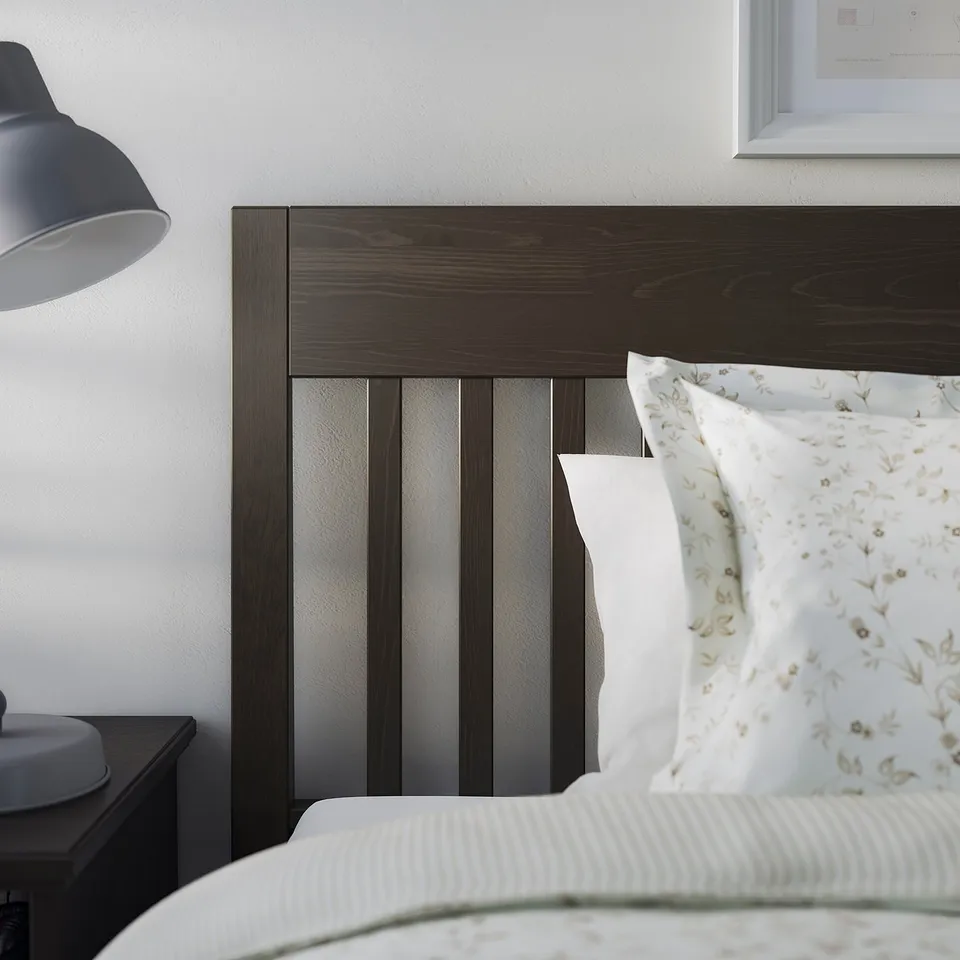 Minimalist bedroom with IDANÄS dark wooden bed, white linens, and grey lampshade.