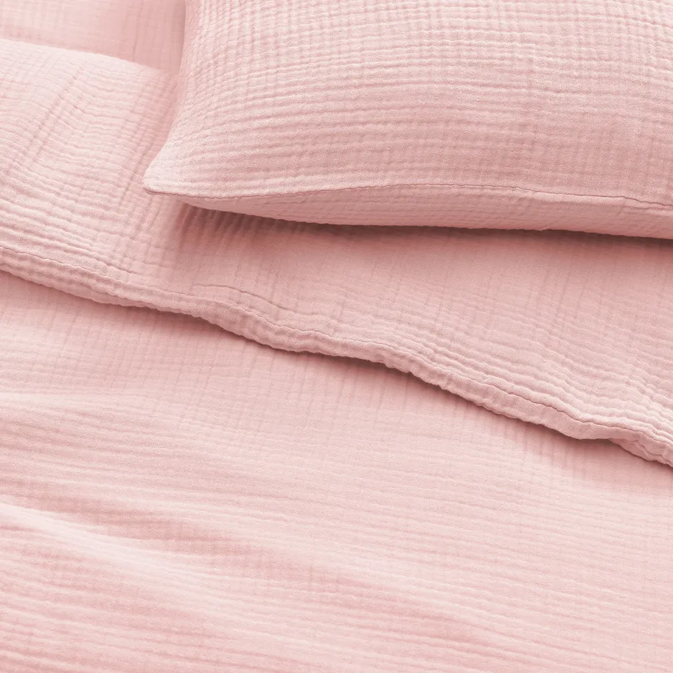 Pile of soft, pink, textured cotton bedding, folded neatly. Shows smooth, even stitching and plush fabric quality.