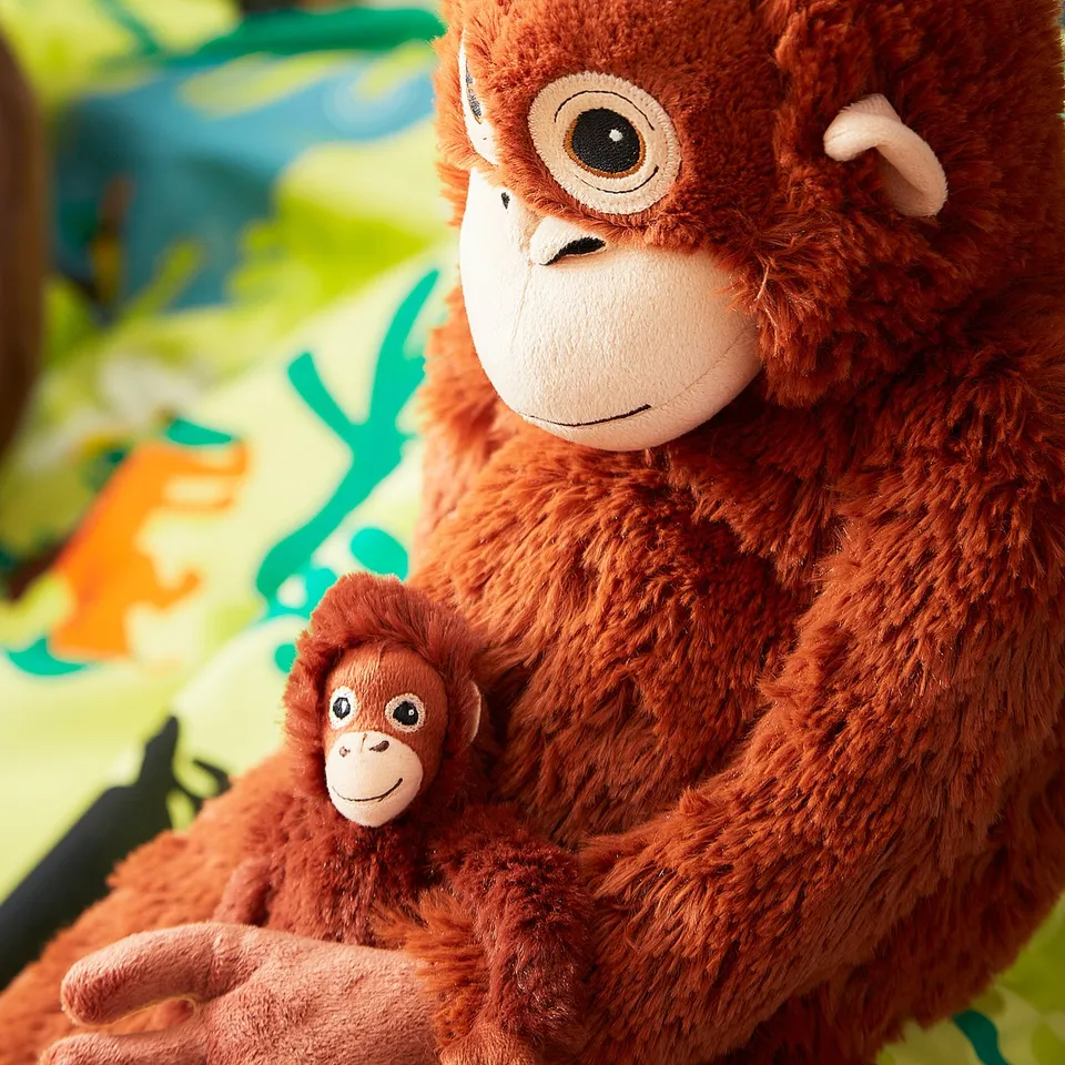 Two brown cuddly toy monkeys, one adult with a baby, sitting on bright green and blue patterned background.