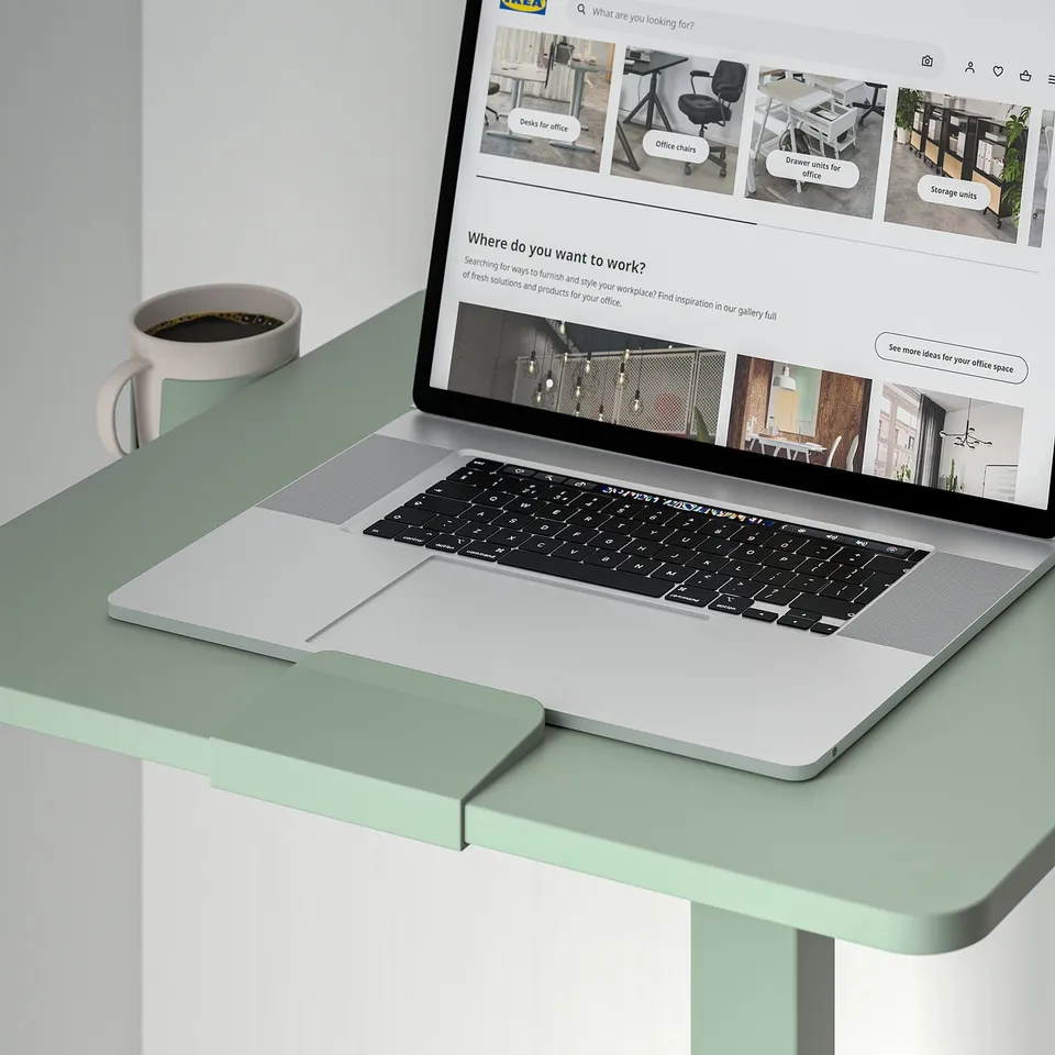 A laptop on a height-adjustable MITTZON desk, shown with a coffee mug holder.
