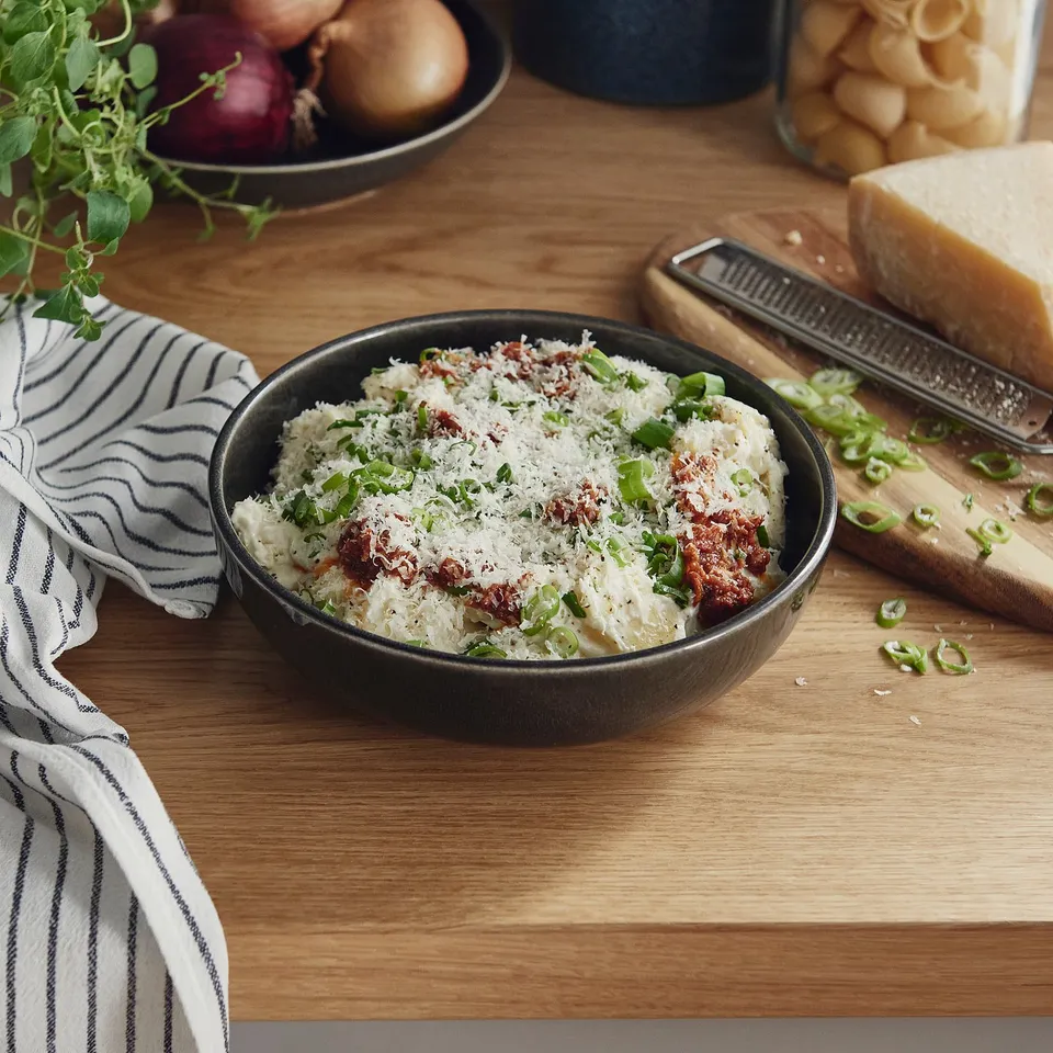 Bowl of creamy dish with cheese, onions, and tomatoes on table.